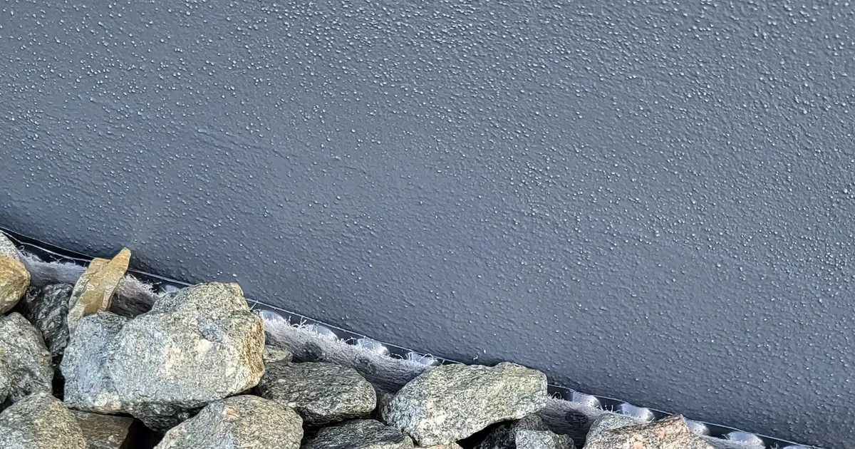 Fertig verlegter Sockelbereich mit Kies-Drainagestreifen: Am Übergang zwischen Sockelputz und Kies ist die helle Vliesschicht der dreilagigen Noppenbahn sichtbar