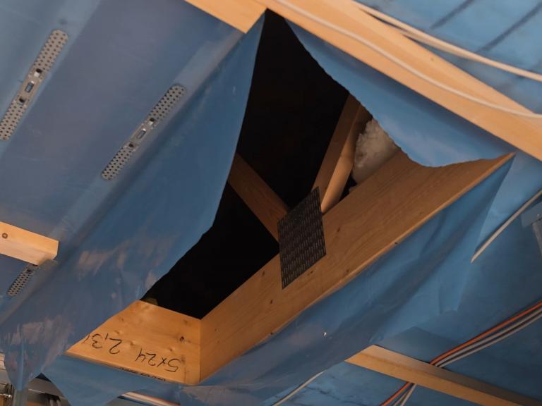 Aufgeschnittene blaue Dampfbremse an einer Öffnung in der Geschossdecke, durch die man in den dunklen, kalten Spitzboden blickt